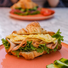 croissant sandwich breakfast with scrambled egg, crispy bacon and mashed avocado.  