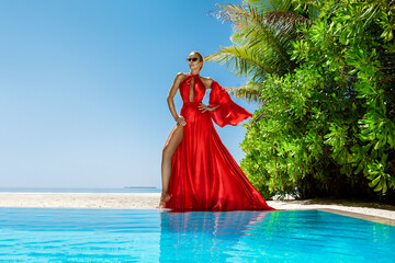 Luxury fashion. Elegant fashion model. Stylish female model in red long gown dress on the Maldives...