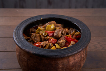 Meat stew with red beans and chili pepper on the table. Hearty beer and lamb stew, with potato, carrot, stewed in a dark beer, with thyme stems, served in a clay pot with irish soda bread on a wooden 