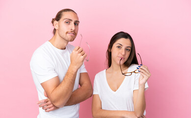 Young caucasian couple isolated on pink background With glasses with happy expression