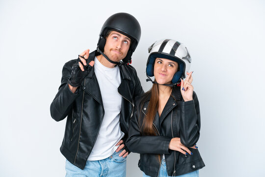 Young caucasian couple with a motorcycle helmet isolated on white background with fingers crossing and wishing the best