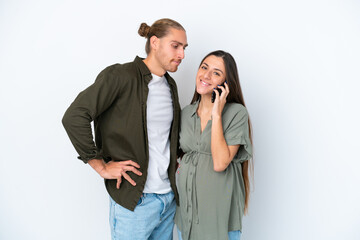 Young caucasian couple isolated on white background pregnant and using mobile phone