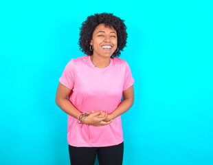 young girl with afro hairstyle wearing pink T-shirt over blue background smiling and laughing hard out loud because funny crazy joke with hands on body.