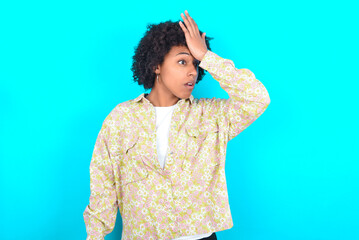 young girl with afro hairstyle wearing floral shirt over blue background surprised with hand on...