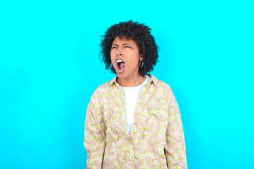 Obraz na płótnie Canvas young girl with afro hairstyle wearing floral shirt over blue background angry and mad screaming frustrated and furious, shouting with anger. Rage and aggressive concept.