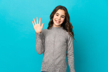Little caucasian girl isolated on blue background saluting with hand with happy expression