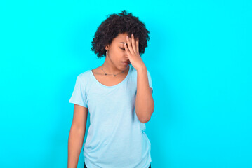 Fototapeta na wymiar Young woman with afro hairstyle wearing blue T-shirt over blue background with sad expression covering face with hands while crying. Depression concept.