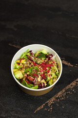 Vegetarian salad with cucumbers, lettuce, walnuts and flax seeds in a round takeaway paper container on dark background.Healthy food, restaurant dish delivery. Top view. Free space for text
