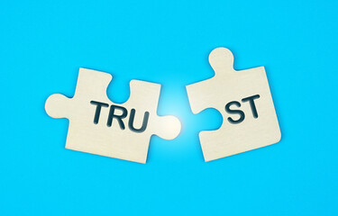Two disconnected puzzle pieces with the word Trust on a blue background. Broken trust, to violate...