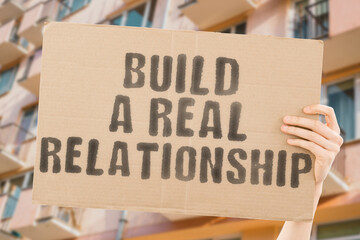 The phrase " Build a real relationship " on a banner in men's hands with blurred background. Join. Professional. Respect. Romance. Romantic. Process. Support. Skill. Promise. Customer. Group. Partner