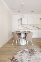 Modern living room interior in pastel colours with round dining table, beige chairs, creamy white kitchen furniture. Trendy minimalistic interior concept