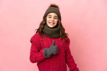 Little girl with winter hat isolated on pink background giving a thumbs up gesture