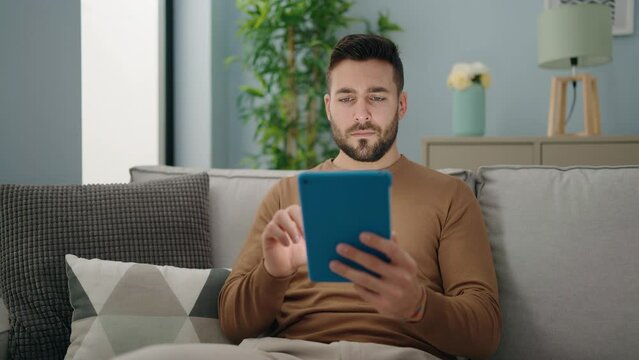 Young hispanic man using touchpad sitting on sofa at home