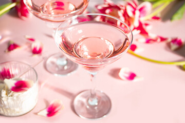 Glasses of pink cocktail with flowers and petals. Birthday party or Valentines day romatic couple concept.
