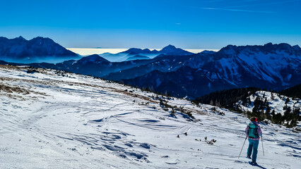 Active woman snow shoe hiking on a trail with scenic view on snow capped mountain peaks of Karawanks in Carinthia, Austria. Ski tour. Julian Alps. Sunny winter day. Freedom. Winter wonderland,Hochobir