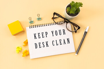KEEP YOUR DESK CLEAN Text written on notepad page, glasses, pen, stationery on yellow background. conceptual image
