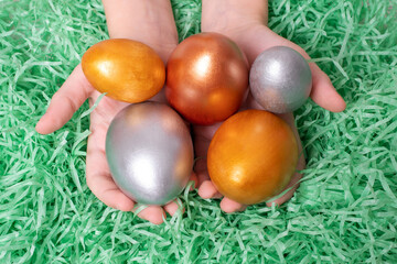 Fototapeta premium Children's hands holding multi-colored eggs on a paper green like grass background. Easter concept