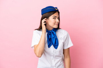 Airplane stewardess Brazilian woman isolated on pink background listening to something by putting hand on the ear