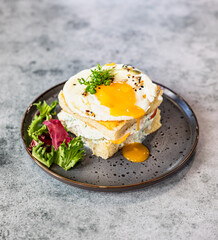 Croque Madame - hot french sandwich with ham, melted cheese, fried egg and sauce with salad. Delicious breakfast.