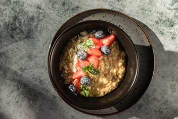 Oatmeal porridge with berries, mint and almond flakes. Trendy photography with bright sunlight and hard shadows. Sunny morning. Healthy breakfast. Top view.