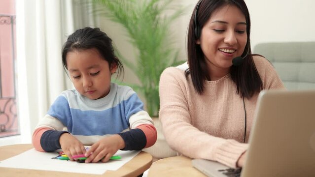 Latin mother working on computer at home with her child - Busy family mom giving call center support