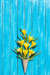 Yellow flowers in ice cream cone on a turquoise wooden background