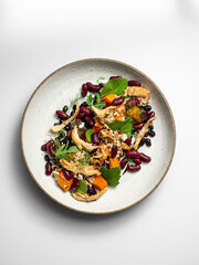 Chicken salad with quinoa, black beans, kidney beans,  pumpkin, fresh herbs. On a ceramic plate, with a white  background