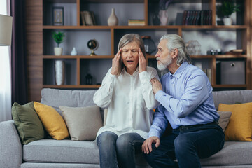 Obraz premium Senior mature man helping her woman with Headache, stress, pain. Old man feeling bad pain disease. Wife supporting husband - Elderly couple suffering migraine depression ache. sitting at home indoors