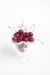 red ripe cherries lie in a transparent vase on a white background