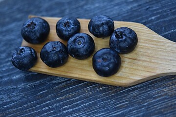 ripe blueberries on a wooden spoon on a dark blue cutting wooden board