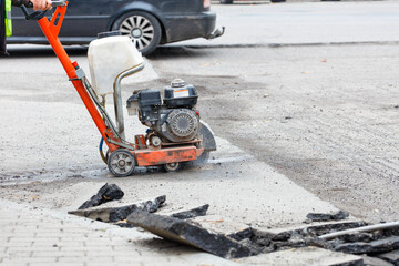 A petrol cutter cuts old asphalt with a diamond wheel, a road worker repairs the carriageway of a city road.