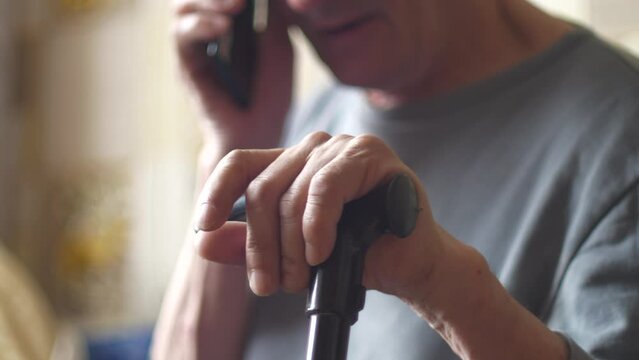 Elderly caucasian man with a walking stick sidf talking on the phone.Lonely old age in a nursing home.The theme of old people.Selective focus, shallow depth of field