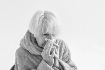 monochrome portrait of senior ill woman freezing cold at home. Health care, crisis, oldness concept