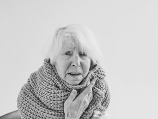 monochrome portrait of senior woman in scarf freezing cold at home. Health care, crisis, oldness...