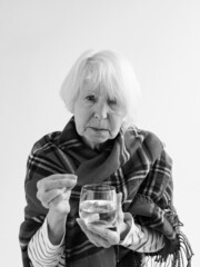 monochrome portrait senior woman in tartan plaid with pill and glass of water. Health care, mature age, illness concept