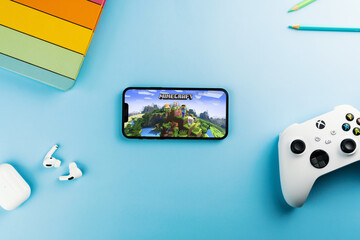 Fototapeta premium Minecraft mobile game app on the smartphone screen. Blue background with school supplies, AirPods, video game controller. Rio de Janeiro, RJ, Brazil. April 2022