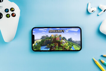 Obraz premium Minecraft mobile game app on the smartphone screen. Blue background with school supplies, AirPods, video game controller. Rio de Janeiro, RJ, Brazil. April 2022