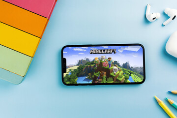 Fototapeta premium Minecraft mobile game app on the smartphone screen. Blue background with school supplies, AirPods, video game controller. Rio de Janeiro, RJ, Brazil. April 2022
