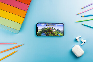 Fototapeta premium Minecraft mobile game app on the smartphone screen. Blue background with school supplies, AirPods, video game controller. Rio de Janeiro, RJ, Brazil. April 2022