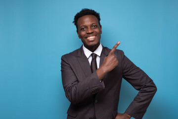 Smiling african man wearing suit looking at camera pointing aside.