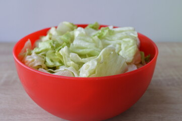 Iceberg lettuce fresh torn salad leaves in a red bowl on wooden  background