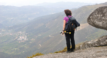 Mulher no topo de uma montanha parada num momento de relaxamento e a observar as vistas do alto - obrazy, fototapety, plakaty