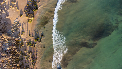 Amazing scenic drone aerial view of the beach and ocean with calm waves during a sunset with vibrant colors. Algarve, Portugal. Clear waters. Holidays and Vacations. Background. Beach with rocks.

