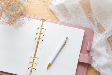 Flat lay, top view of a pastel pink leather planner, dried flower bouquet and stationery on a wooden desk.