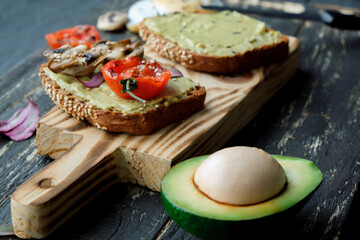 Avocado toast with grilled tomatoes and grilled mushrooms on dark wooden table. Healthy food and vegan diet concepts