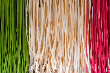 Handmade uncooked fettuccine wheat pasta of three colors white, red, and green like the Italian flag
