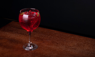 red cherry cocktail glass with gin rosemary lemon and ice in angle view wooden table
