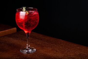 red cocktail glass with lemon rosemary gin and ice on corner wooden table