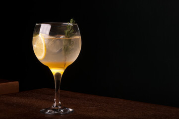 Sicilian lemon tropical cocktail glass with rosemary gin and ice in front view wooden table and dark background