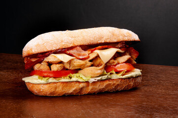 sub sandwich of chicken cubes bacon lettuce tomato mayonnaise on italian baguette on wooden table...
